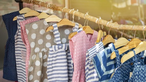 Kidss fashion, cute little girl dress hanging on wooden stick over blurred cloth shop background