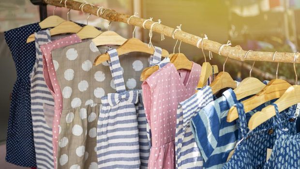 Kids's fashion, cute little girl dress hanging on wooden stick over blurred cloth shop background