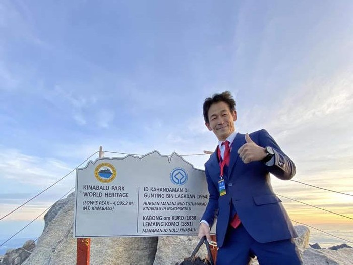 Pria Jepang mendaki Gunung Kinabalu mengenakan setelan jas.