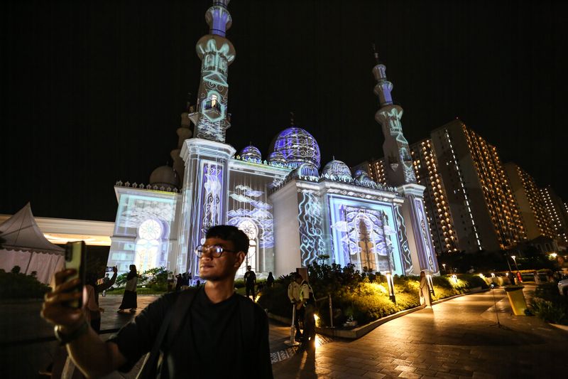 Pengunjung berswafoto dengan latar belakang video mapping yang ditampilkan saat acara Khazanah Fest di Masjid At-Thohir, Depok, Jawa Barat, Minggu (2/4/2023). Masjid At-Thohir yang dibangun sejak tahun 2022 dengan gaya arsitektur klasik modern tersebut menampilkan pertunjukkan video mapping nuansa Ramadhan. ANTARA FOTO/Asprilla Dwi Adha/YU