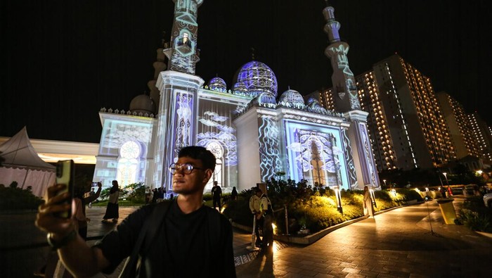 Pengunjung berswafoto dengan latar belakang video mapping yang ditampilkan saat acara Khazanah Fest di Masjid At-Thohir, Depok, Jawa Barat, Minggu (2/4/2023). Masjid At-Thohir yang dibangun sejak tahun 2022 dengan gaya arsitektur klasik modern tersebut menampilkan pertunjukkan video mapping nuansa Ramadhan. ANTARA FOTO/Asprilla Dwi Adha/YU