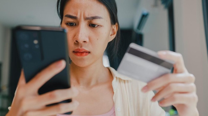 Close-up Youth asia female wear casual sit front of desk hold smartphone and credit card feel upset online shopping payment declined credit over limit in living room at house. Home lifestyle concept.