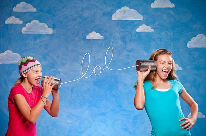 Ilustasi anak Jaksel ngomong bahasa gaul Inggris. A ten and thirteen year old girls speaking on tin can telephones, The string spells LOL, laugh out loud or lots of love. This shot was done in the studio in fron tof a painted cloud background.