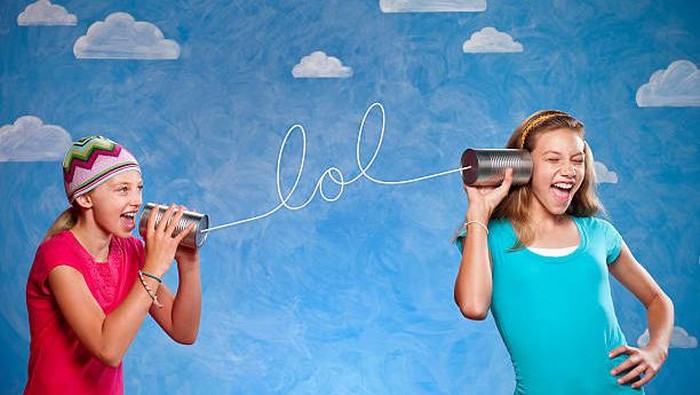 A ten and thirteen year old girls speaking on tin can telephones, The string spells LOL, laugh out loud or lots of love. This shot was done in the studio in fron tof a painted cloud background.