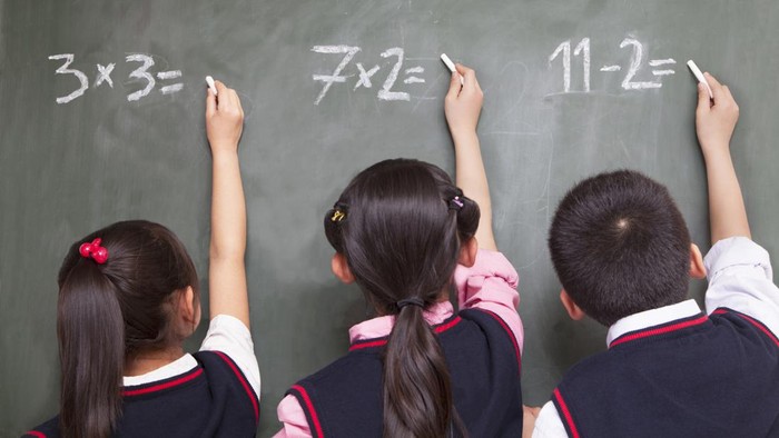 Three school children doing math equations on the blackboard