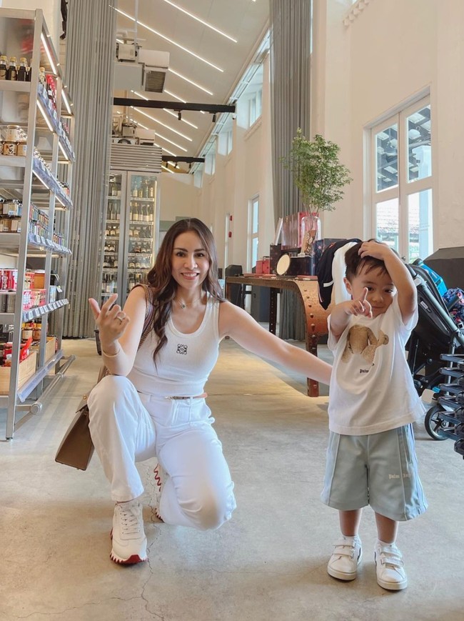 Dalam foto terlihat Momo memadukan atasan tanktop putih dengan celana panjang dan sepasang sepatu berwarna senada. Penampilannya itu tampak kompak dengan sang anak yang juga mengenakan kaos dan sepatu berwarna putih. Foto: Instagram/@therealmomogeisha