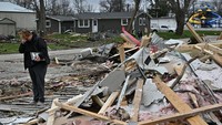 Jodee Minks memegang memorabilia dan menangis sambil melihat sekolah miliknya yang hancur sehari setelah tornado menghantam Sullivan, Indiana, AS, 1 April 2023. REUTERS/Jon Cherry.