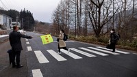 Kepala SMP Yumoto, Watanabe, melambaikan bendera kuning sebagai peringatan untuk menyeberang jalan bagi para murid terakhirnya, Eita dan Aoi yang tiba di sekolah SMP Yumoto pada 10 Maret 2023 lalu.Foto: REUTERS/ISSEI KATO
