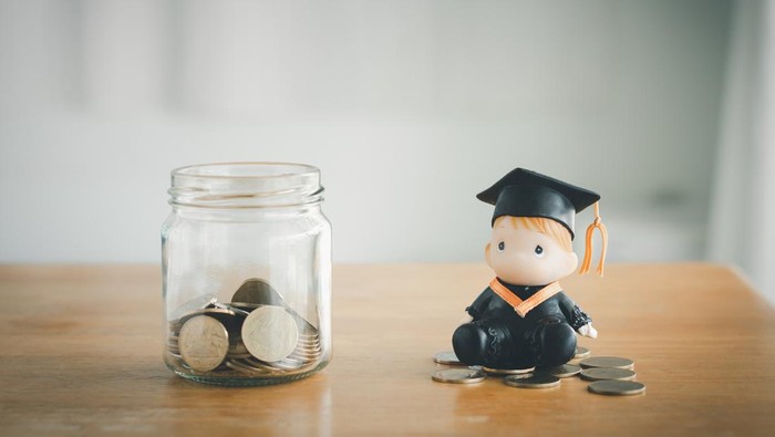 Education savings concept. Coins in a glass jar for education money savings with a graduate doll. Personal financial planning for the future.