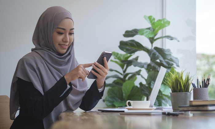 Ilustrasi wanita hijab pakai ponsel dan laptop