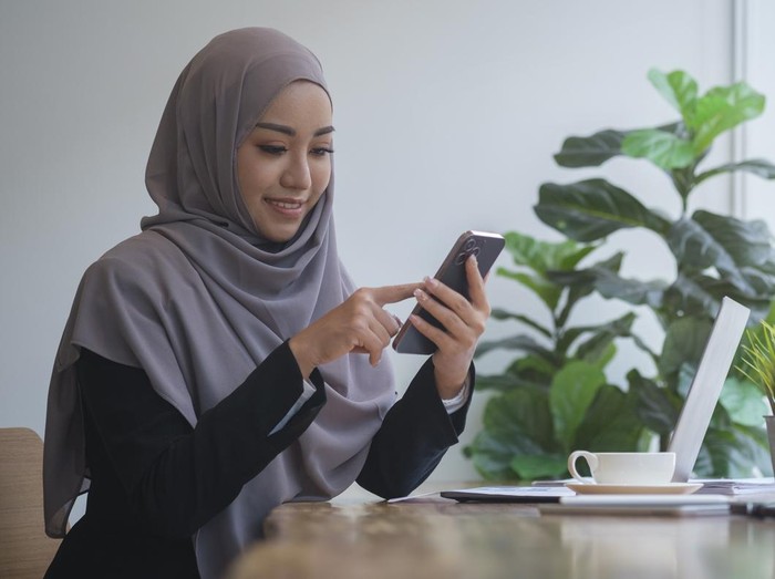 Ilustrasi wanita hijab pakai ponsel dan laptop