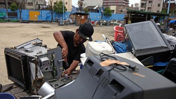 Seorang pria bekerja mengumpulkan komponen dari barang elektronik bekas. Foto: Getty Images