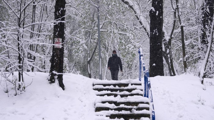 A man walks through a snow covered park in Belgrade, Serbia, Tuesday, April 4, 2023. An unusual occurrence of winter-like weather in spring swept through the Western Balkans Tuesday, bringing snow and gusts that have snarled traffic in the region. (AP Photo/Darko Vojinovic)