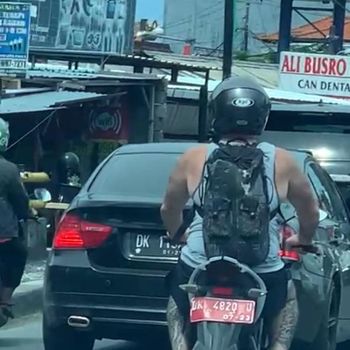 Tangkapan layar seorang WNA mengendarai sepeda motor pelat merah nomor polisi DK 4820 U viral di media sosial.