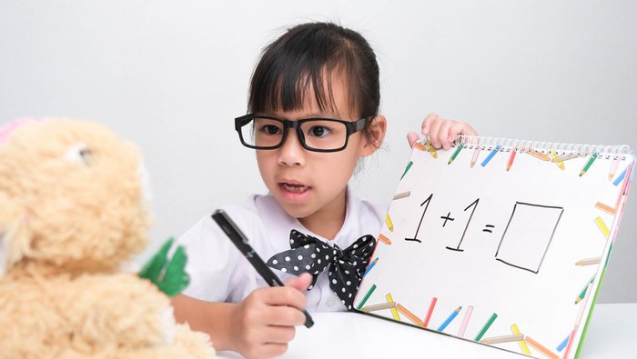 Cute Asian little girl playing teacher role game. A little girl is teaching math to her teddy bear friend. Homeschool childrens play and learning.