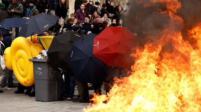 Masked protesters protect themselves with umbrellas near burning garbage bins amid clashes during a demonstration as part of the eleventh day of nationwide strikes and protests against French government's pension reform, in Rennes, France, April 6, 2023.  REUTERS/Stephane Mahe