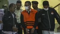 Dia tampak mengenakan rompi tahanan berwarna oranye.