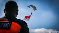 Penerjun payung membawa bendera Indonesia, TNI, dan TNI AU dari atas langit. 