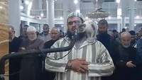 Malahan, dirinya mengelus dan memegangi kucing tersebut saat memanjat tubuhnya. Si kucing yang lugu itu sempat duduk di pundak sang imam, lalu mendekatkan wajahnya ke arah mik seolah ingin meongannya terdengar seluruh jemaah. (Foto: Facebook/The Official Page of the Reciter Walid Mehsas)