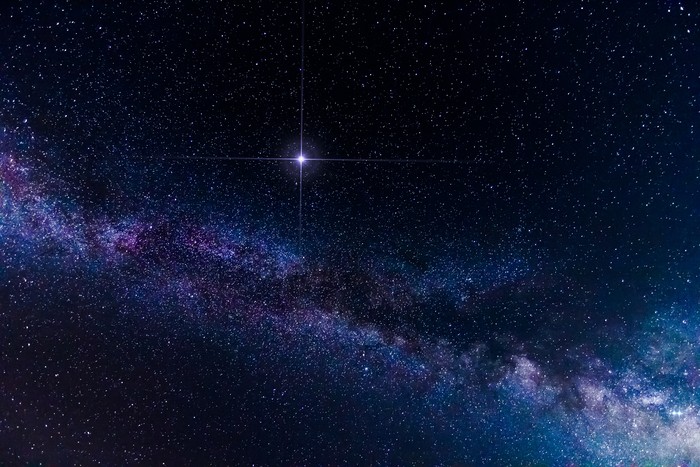 Beautiful spike glowing lucky star and Milky Way Galaxy in all its beauty es seen on a clear dark night during summer in Northern Hemisphere from Europe. Long exposure for 30 seconds, shot on Canon EOS camera. Intense shining star is added in post edit via software enhancement of an actual star on the dark sky.