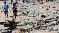 Anak-anak berjalan melewati plastik dan sampah lainnya yang terdampar di Pantai Kedonganan, Kabupaten Badung, di pulau resor Bali, Indonesia pada 12 April 2023.