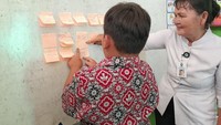 Sementara Muel menulis huruf di meja, Hani mengecek hasil tulisan Bawe dan kawan-kawan. Ada yang masih keliru satu-dua huruf, ada yang menggunakan huruf kapital di tengah kalimat, ada juga yang sudah rapi menulis dengan baik dan benar sesuai EYD. Foto: Trisna Wulandari/detikEdu