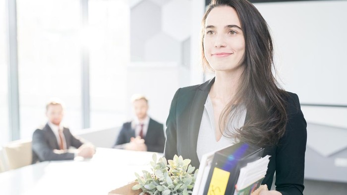 Waist up portrait of smiling young businesswoman holding box of personal belongings  leaving office after quitting job, copy space