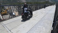 Pengendara sepeda motor melintasi jembatan darurat yang dipasang pada badan jembatan yang ambles di Kelurahan Buluri di Palu, Sulawesi Tengah, Kamis (13/4/2023).