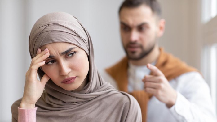 Husband Shouting At Depressed Wife Tired Of Domestic Violence And Victimization Standing At Home. Selective Focus. Relationship With Abuser And Family Conflicts