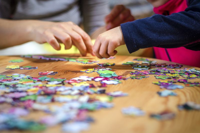 Ilustrasi Aktivitas Edukatif saat Libur Lebaran Hands of a little child and parent plying jigsaw puzzle game on a wooden table