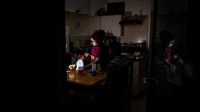 Krisis Energi Bikin Ramadan di Afrika Selatan Gelap Gulita The family of Zulfaqaar Seedat (L) and Kurshaid Shaik (R) use portable lamps to brighten their kithchen during rolling blackouts while sharing a meal at the time of Sehri (also called Suhoor), the meal consumed early in the morning by Muslims during the month of Ramadan before sunrise, in Robertsham, Johannesburg, on 12 April 2023. - Scheduled blackouts, known as loadshedding, have burdened Africa's most industrialised economy for years, with its state-owned energy firm Eskom failing to keep pace with demand and maintain its ageing coal power infrastructure. (Photo by Shiraaz Mohamed / AFP) (Photo by SHIRAAZ MOHAMED/AFP via Getty Images)