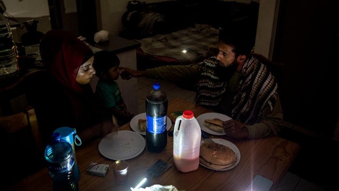 Krisis Energi Bikin Ramadan di Afrika Selatan Gelap Gulita The family of Zulfaqaar Seedat (L) and Kurshaid Shaik (R) use portable lamps to brighten their kithchen during rolling blackouts while sharing a meal at the time of Sehri (also called Suhoor), the meal consumed early in the morning by Muslims during the month of Ramadan before sunrise, in Robertsham, Johannesburg, on 12 April 2023. - Scheduled blackouts, known as loadshedding, have burdened Africa's most industrialised economy for years, with its state-owned energy firm Eskom failing to keep pace with demand and maintain its ageing coal power infrastructure. (Photo by Shiraaz Mohamed / AFP) (Photo by SHIRAAZ MOHAMED/AFP via Getty Images)