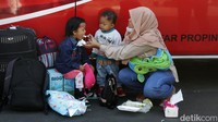 Seorang ibu menunggu jadwal keberangkatan sambil menyuapi anaknya di samping bus AKAP. 