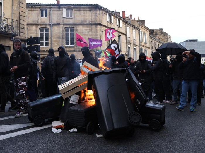 Protesters walks past burning bins during a demonstration after Frances Constitutional Council approved the key elements of a pension reform, in Bordeaux, southwestern France, on April 14, 2023. - France has been rocked by three months of demonstrations and strikes over the presidents bid to raise the retirement age to 64 from 62, with around two in three voters against the changes, according to polls. The government on March 16 pushed a pensions reform through parliament without a vote, using the article 49.3 of the constitution. (Photo by Thibaud MORITZ / AFP)