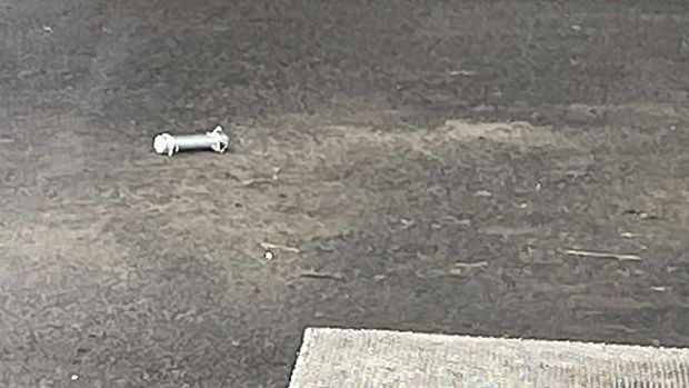 A cylinder-shaped object (L), believed to have been thrown during Japan's Prime Minister Fumio Kishida's campaign, is seen on the ground in Wakayama on April 15, 2023. - Kishida was evacuated from a port in Wakayama after a blast was heard, but he was unharmed in the incident, local media reported on April 15. (Photo by JIJI Press / AFP) / Japan OUT