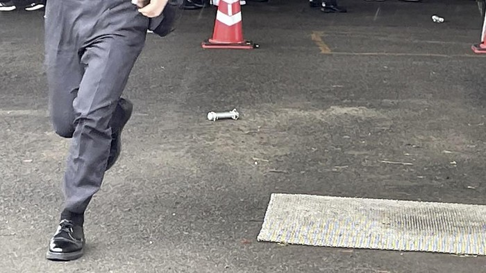 A cylinder-shaped object (C), believed to have been thrown during Japans Prime Minister Fumio Kishidas campaign, is seen on the ground in Wakayama on April 15, 2023. - Kishida was evacuated from a port in Wakayama after a blast was heard, but he was unharmed in the incident, local media reported on April 15. (Photo by JIJI Press / AFP) / Japan OUT