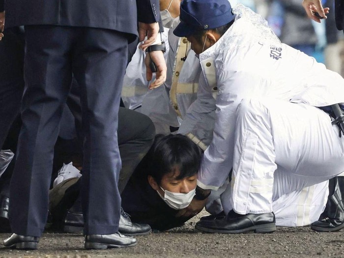A man, believed to be a suspect who threw a pipe-like object near Japanese Prime Minister Fumio Kishida during his outdoor speech, is held by police officers at Saikazaki fishing port in Wakayama, Wakayama Prefecture, south-western Japan April 15, 2023, in this photo released by Kyodo. Mandatory credit Kyodo via REUTERS