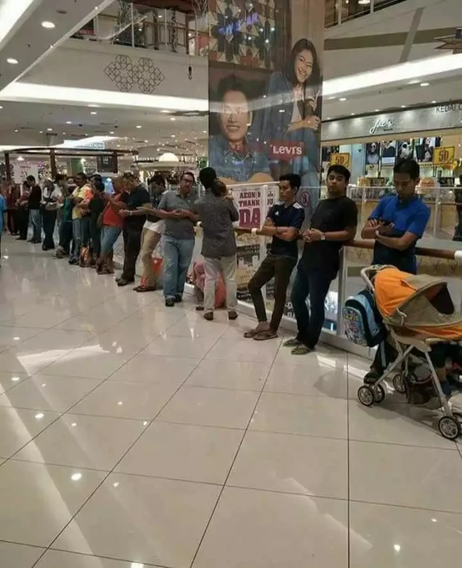 Ini namanya barisan para bapak penunggu istri. Terlihat betapa gabutnya para bapak-bapak. Beberapa ada yang sambil momong anak. Foto: Facebook/KataKita