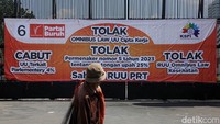 Pejalan kaki melitas di depan gerbang Gedung DPR yang dipasangi baliho penolakan UU Cipta Kerja.