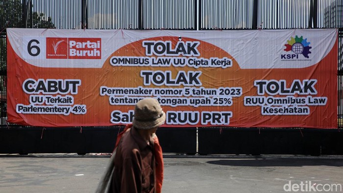 Gerbang DPR Dipasangi Baliho Tolak UU Cipta Kerja Pejalan kaki melitas dekat gerbang komplek parlemen DPR RI yang dipasangi baliho penolakan UU Cipta Kerja , Jakarta, Senin (17/4/2023). Partai Buruh menolak UU Cipta Kerja, selanjutnya para buruh menuntut pemerintah mencabut parliamentary threshold atau ambang batas parlemen. mereka juga menuntut agar DPR segera mengesahkan RUU Perlindungan Pekerja Rumah Tangga (PPRT) menjadi Undang-Undang