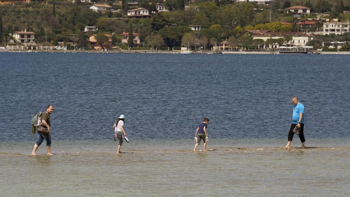 Potret Italia Kekeringan Parah, Wisatawan Sampai Bisa Seberangi Pulau Jalan Kaki Tourists cross a stretch between the mainland and the San Biagio island in Manerba, on the Garda Lake, Italy, Friday, April 14, 2023. (AP Photo/Luca Bruno)