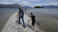 Wisatawan menyeberangi bentangan antara daratan dan pulau San Biagio di Manerba, di Danau Garda, Italia, Jumat (14/4/2023). Wisatawan tidak lagi memerlukan perahu untuk mencapai pulau di Italia ini karena alam telah meciptakan jalan setapak.