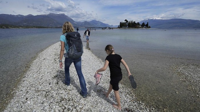 Tourists cross a stretch between the mainland and the San Biagio island in Manerba, on the Garda Lake, Italy, Friday, April 14, 2023. (AP Photo/Luca Bruno)