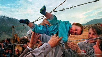 Carol Guzy, wanita pertama yang menerima Hadiah Pulitzer untuk fotografi berita spot. Dia menerima Pulitzer terbarunya pada tahun 2000 untuk foto-fotonya yang menyentuh tentang pengungsi Kosovo. Gambar di atas menggambarkan Agim Shala, seorang bocah lelaki berusia dua tahun, yang melewati pagar yang terbuat dari kawat berduri ke keluarganya. Ribuan pengungsi Kosovo dipersatukan kembali dan berkemah di Kukes, Albania. Foto: via steemit