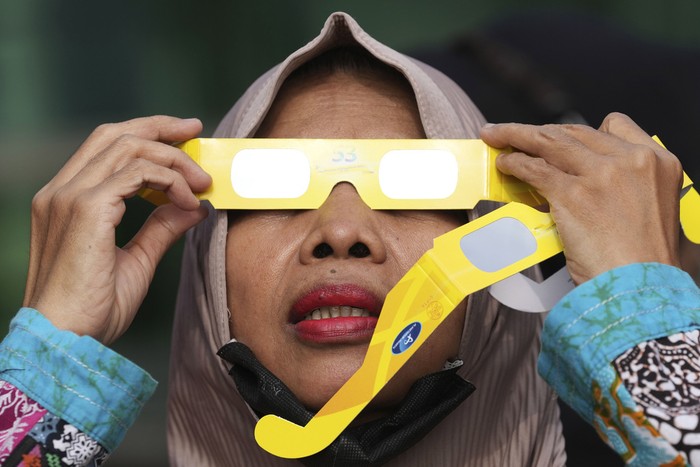 People use protective glasses to watch solar eclipse in Jakarta, Indonesia, Thursday, April 20, 2023. A rare solar eclipse will cross over remote parts of Australia, Indonesia and East Timor on Thursday. (AP Photo/Tatan Syuflana)