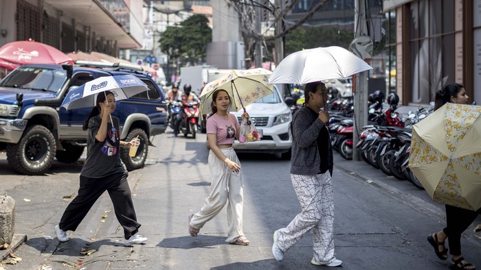 People sheltering from the sun under umbrellas cross a street during heatwave conditions in Bangkok on April 20, 2023. - Sweltering under a blistering sun, people across South and Southeast Asia have been taking cover beneath any shelter they can find as they pray for cooling rains with record temperatures hitting the region. (Photo by Jack TAYLOR / AFP)