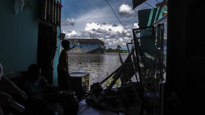 Seorang bocah melihat kapal tongkang melintas di belakang rumahnya yang rusak di Desa Keladan, Kabupaten Tapin, Kalimantan Selatan, Minggu (23/4/2023).Dua kapal tongkang pengangkut batu bara milik perusahaan PT Rimau Bahtera Shiping dan PT Batu Gunung Mulia Energi menabrak sebanyak 35 rumah dan puluhan alat transportasi air milik warga di permukiman padat penduduk, penyebab diduga akibat angin deras pada Sabtu (22/4/2023) sore. ANTARA FOTO/Bayu Pratama S/rwa.