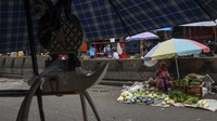 Seorang pedagang sayur menunggu pembeli di tepi jalan.