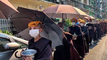 Biarawati Budha mengumpulkan sedekah dengan kepala ditutupi handuk dan memakai payung untuk berlindung dari matahari selama gelombang panas di Yangon pada 24 April. Gelombang panas April terburuk dalam sejarah Asia berlangsung di lebih dari selusin negara. Foto: AFP via Getty Images/SAI AUNG MAIN