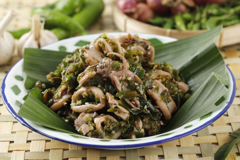 Close Up Cumi Cabe Ijo, Spicy Stir Fry Squid with Green Pepper, Shallot, and Garlic. Served on Enamel Plate on Wooden Table